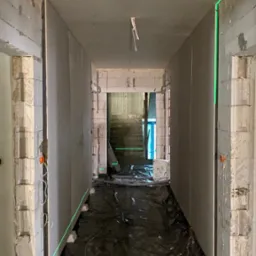 Korytarz w trakcie remontu: widoczne płyty karton gips na ścianach, poziomy laserowy wyznaczający płaszczyznę, podłoga zabezpieczona folią malarską.