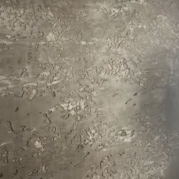 ,,BRODA-BUD” PRZEMYSŁAW MASTERNAK - Szara ściana z nieregularną, chropowatą fakturą imitującą naturalny kamień lub beton, z widocznymi smugami i wgłębieniami.