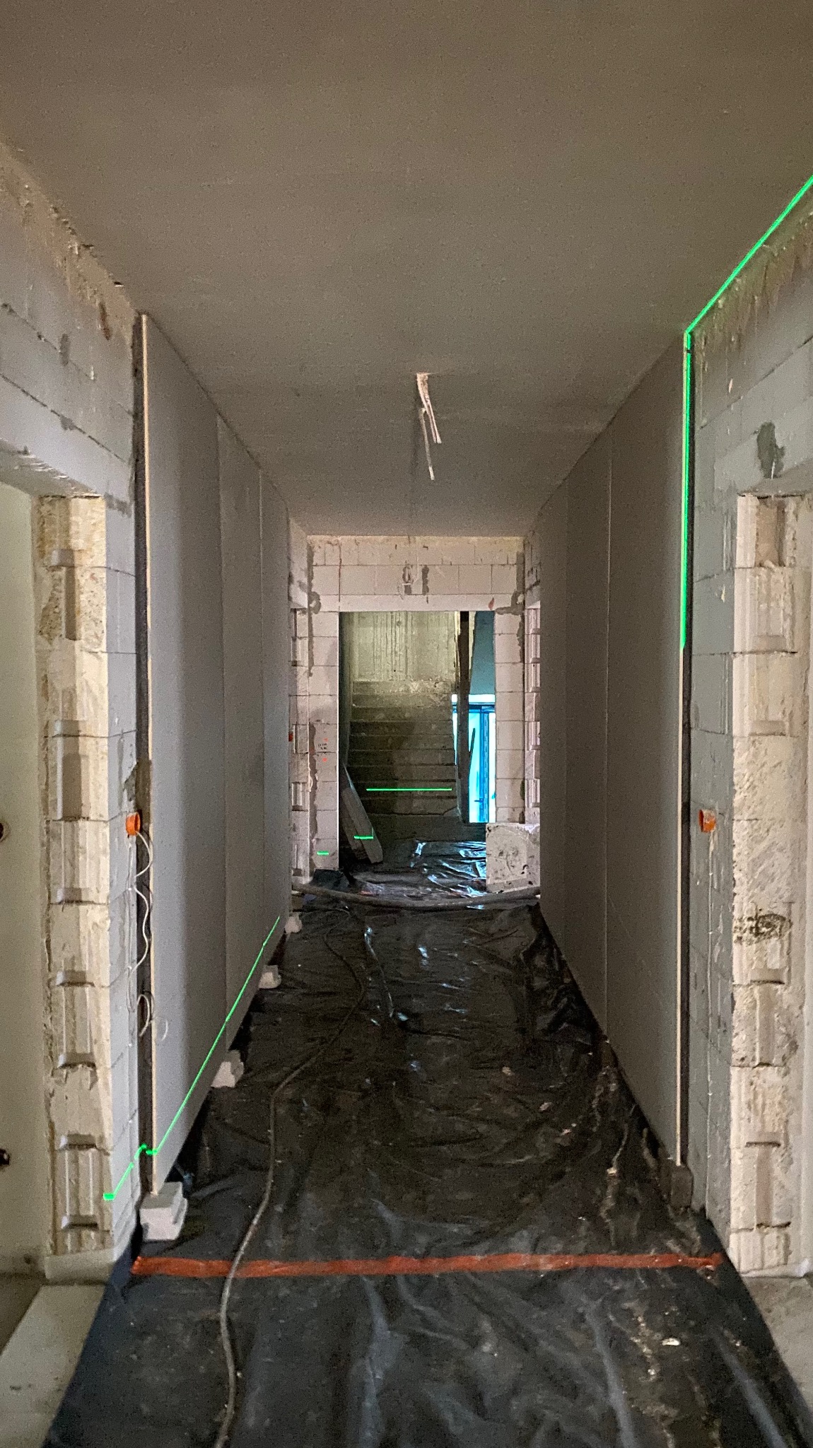 Korytarz w trakcie remontu: widoczne płyty karton gips na ścianach, poziomy laserowy wyznaczający płaszczyznę, podłoga zabezpieczona folią malarską.
