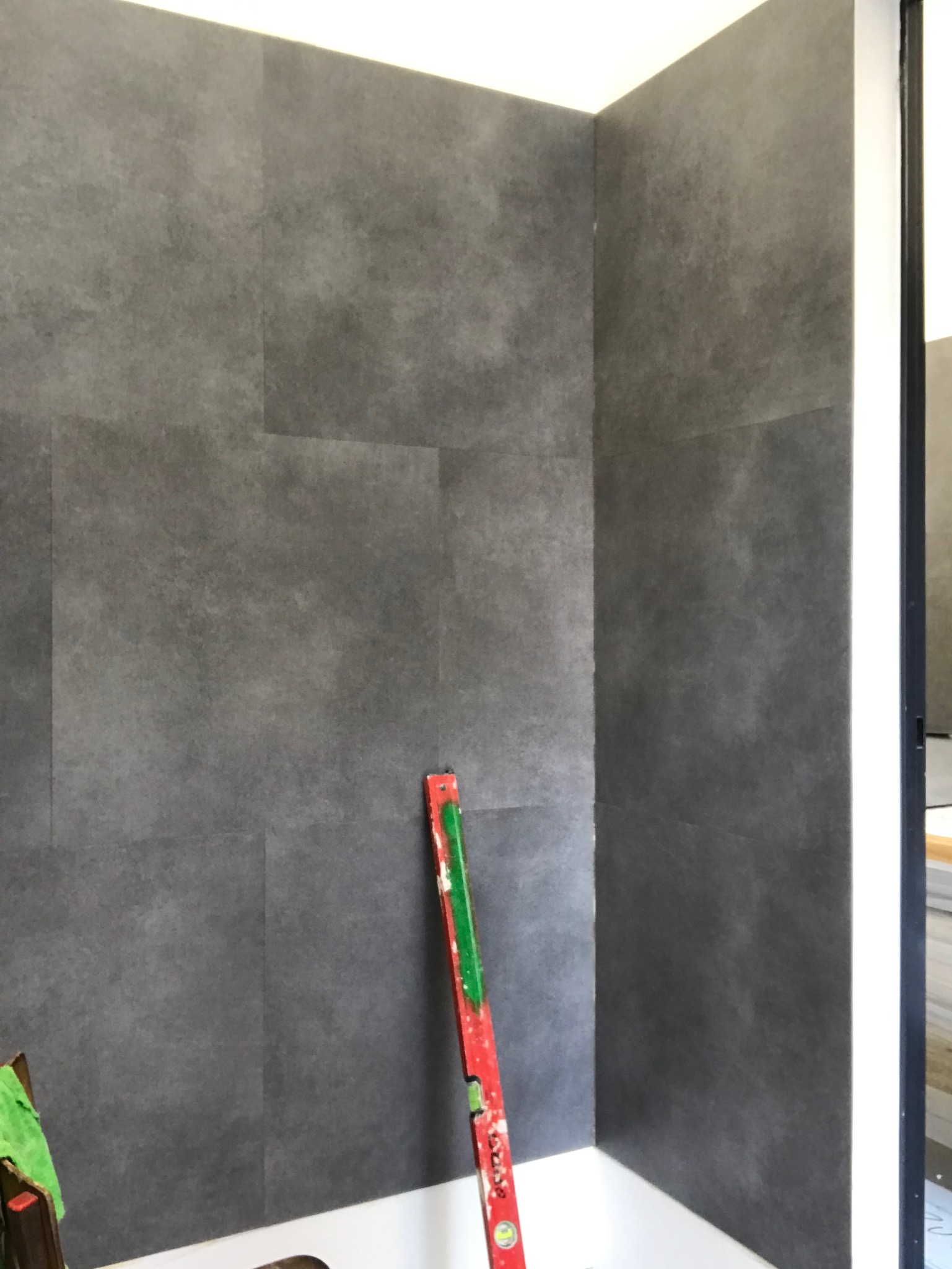 Montaż szarych paneli ściennych w rogu pomieszczenia, poziomica w kolorach czerwieni i zieleni oparta o ścianę, widoczny fragment drabiny.