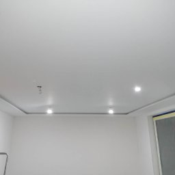 IDEA HOUSE Przemysław Jurzec - Białe wnętrze po odświeżeniu: widoczne gładkie ściany, sufit z oświetleniem punktowym i zabezpieczone folią okno, drabina w rogu.