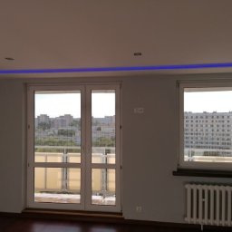 IDEA HOUSE Przemysław Jurzec - Wnętrze pokoju po remoncie z oknem balkonowym i grzejnikiem. Sufit ozdobiony niebieskim oświetleniem LED.