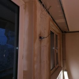 IDEA HOUSE Przemysław Jurzec - Wnętrze w trakcie przygotowań do malowania: ściany po nałożeniu gładzi gipsowej, widoczne przewody elektryczne, zamontowane profile sufitowe, okno z białymi ramami.