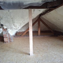 IDEA HOUSE Przemysław Jurzec - Poddasze w trakcie ocieplania pianą PUR, widoczne krokwie, mur z czerwonej cegły i drewniana podłoga z płyt OSB.