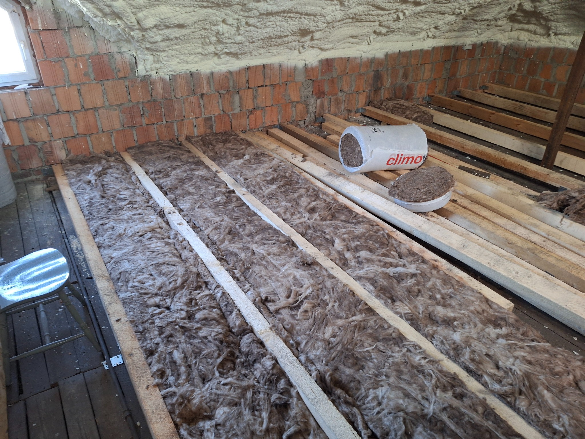 Ocieplenie poddasza wełną mineralną między legarami, widoczny fragment ściany z czerwonej cegły i puszka z wełną mineralną marki Climawool