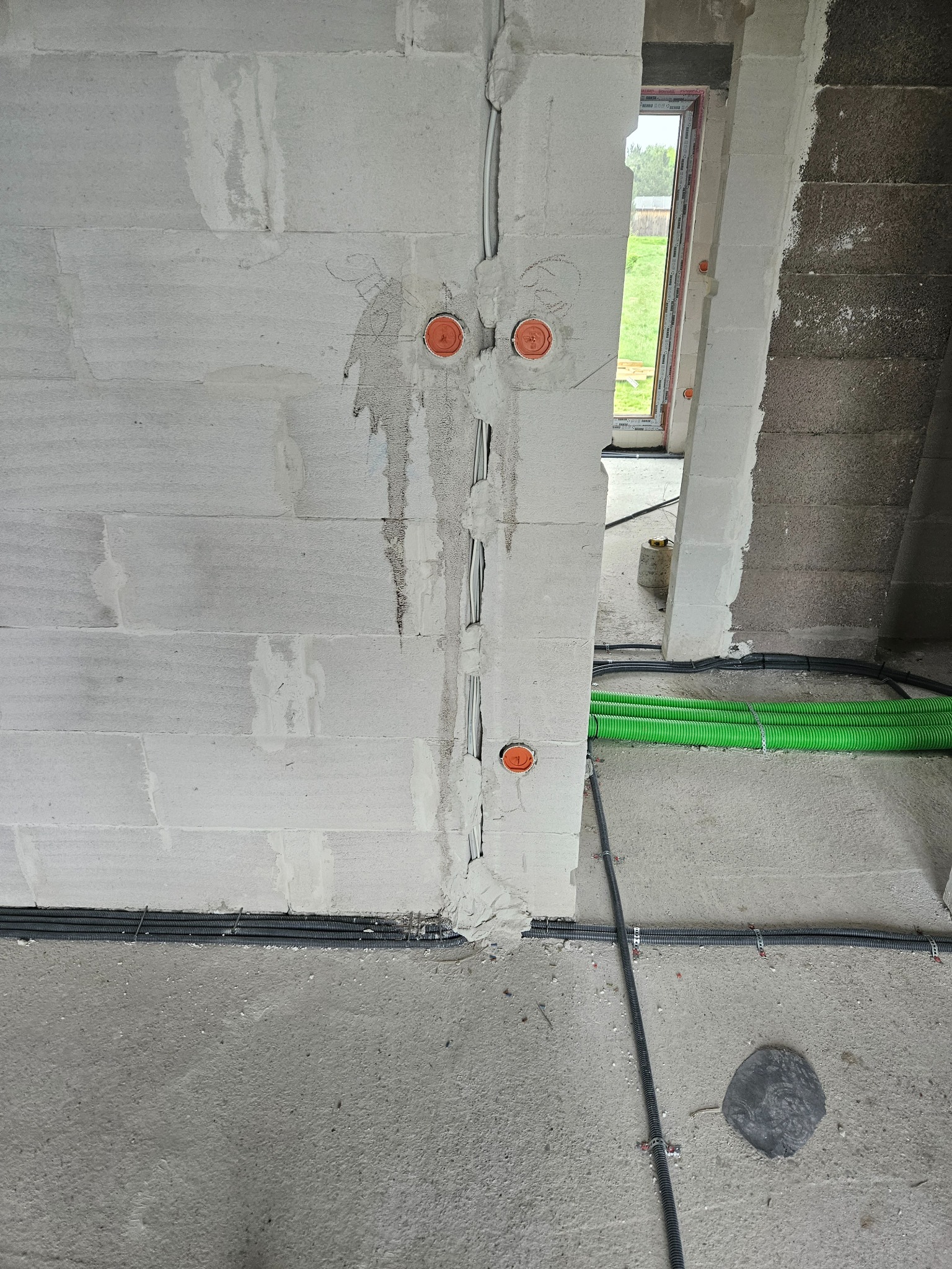 Wewnętrzne okablowanie elektryczne w ścianie z betonu komórkowego z pomarańczowymi puszkami instalacyjnymi, widoczne przewody w peszlach i rurach instalacyjnych, etap prac instalacyjnych w surowym...