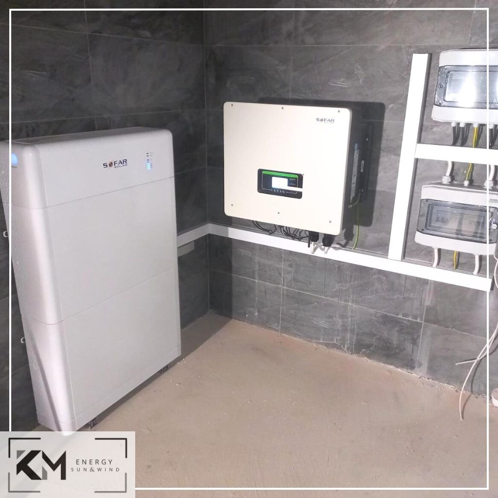 Biały magazyn energii Sofar obok białego inwertera Sofar zamontowanego na szarej, kafelkowej ścianie w pomieszczeniu technicznym. Obok widoczne skrzynki elektryczne.