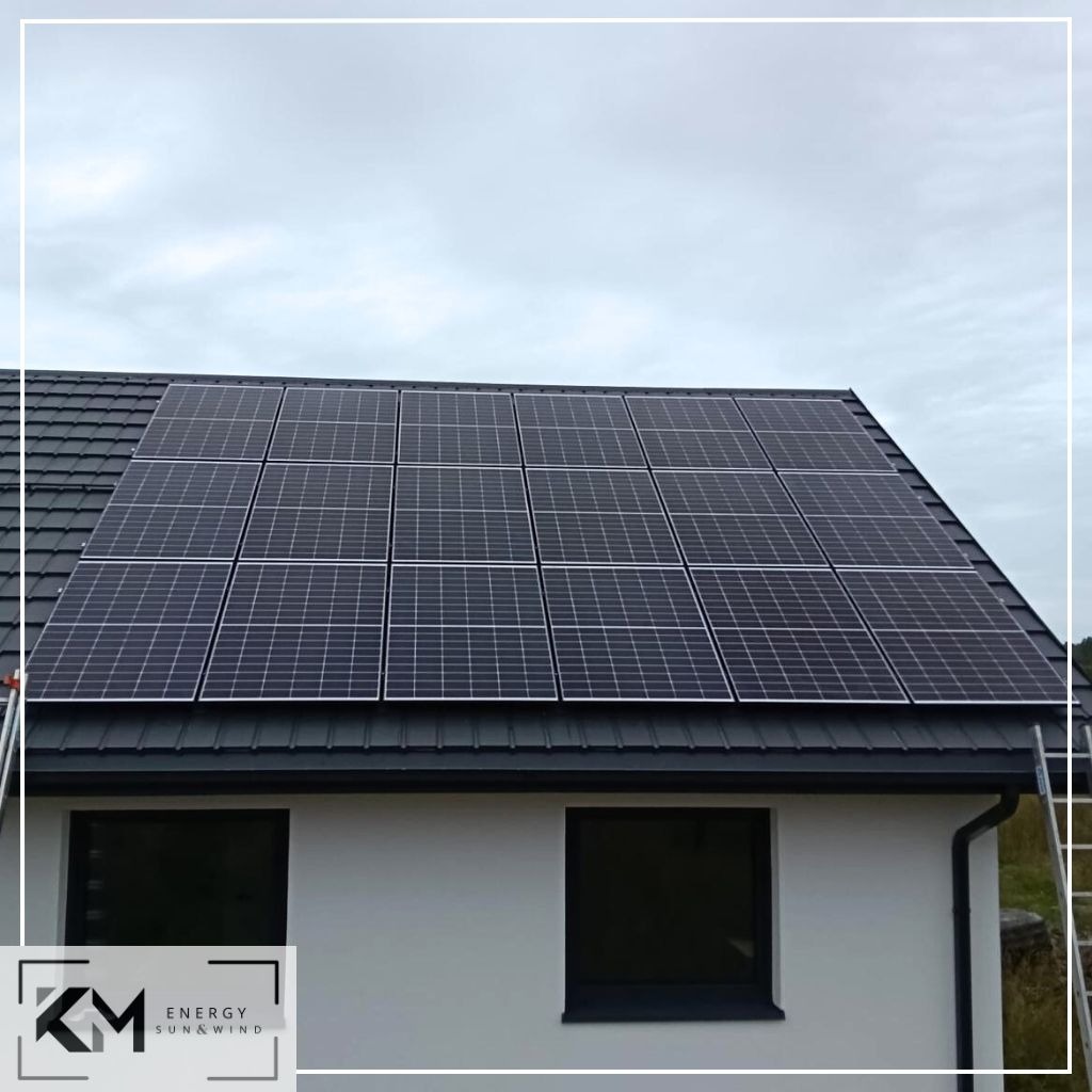 Panele słoneczne na dachu domu jednorodzinnego z szarą dachówką, drabina oparta o rynnę, pochmurne niebo.