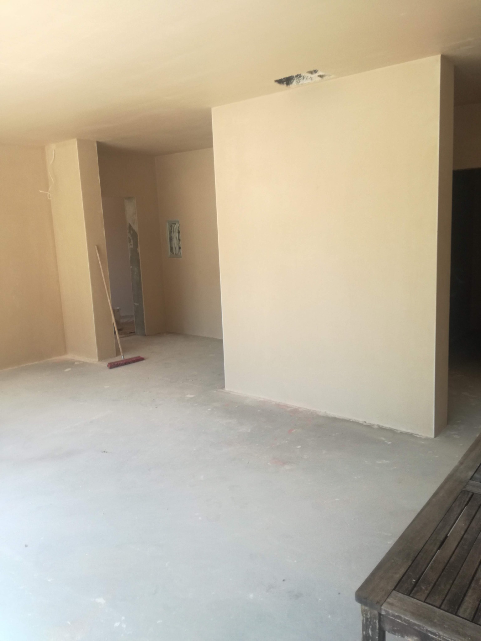 Wnętrze po nałożeniu jasnobeżowych gładzi. Widoczne ściany, sufit, podłoga i częściowo meble. Na podłodze leży miotła.