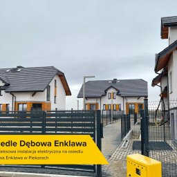 FUTUREL SPÓŁKA Z OGRANICZONĄ ODPOWIEDZIALNOŚCIĄ - Nowoczesne osiedle domów jednorodzinnych z szarą dachówką i grafitowymi ogrodzeniami panelowymi, widoczna skrzynka elektryczna w kolorze żółtym oraz kable wystające z elewacji jednego z domów.
