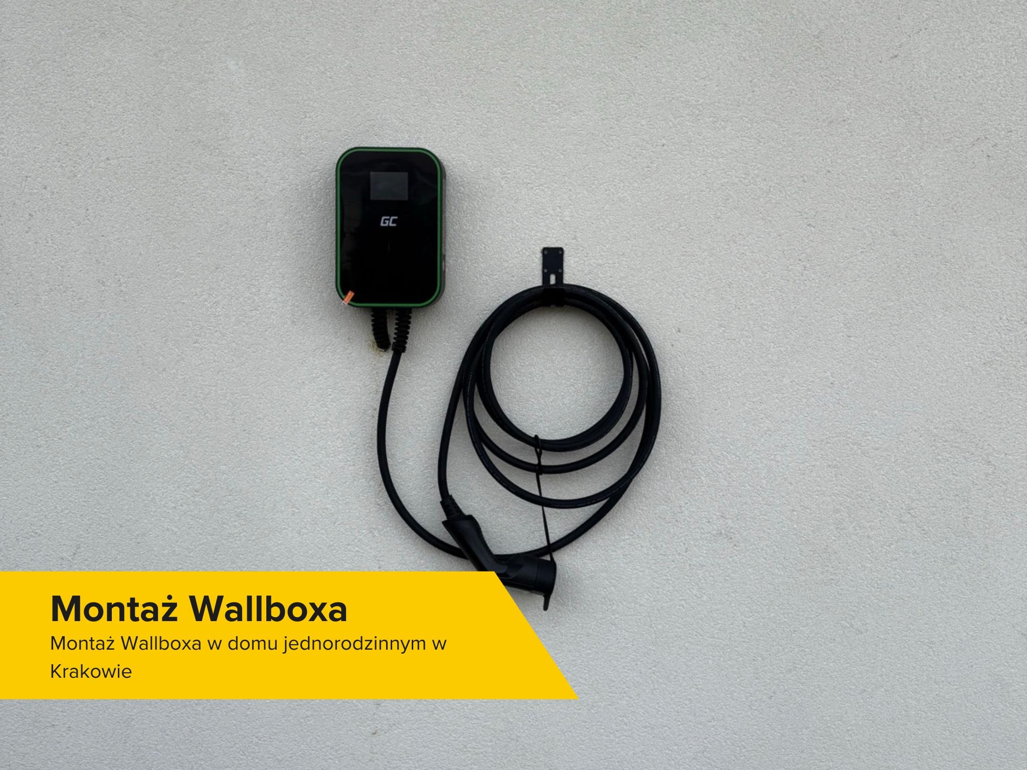 Czarny wallbox marki GC zamontowany na jasnej, zewnętrznej ścianie budynku, kabel zwinięty w pętlę, widoczny uchwyt mocujący.