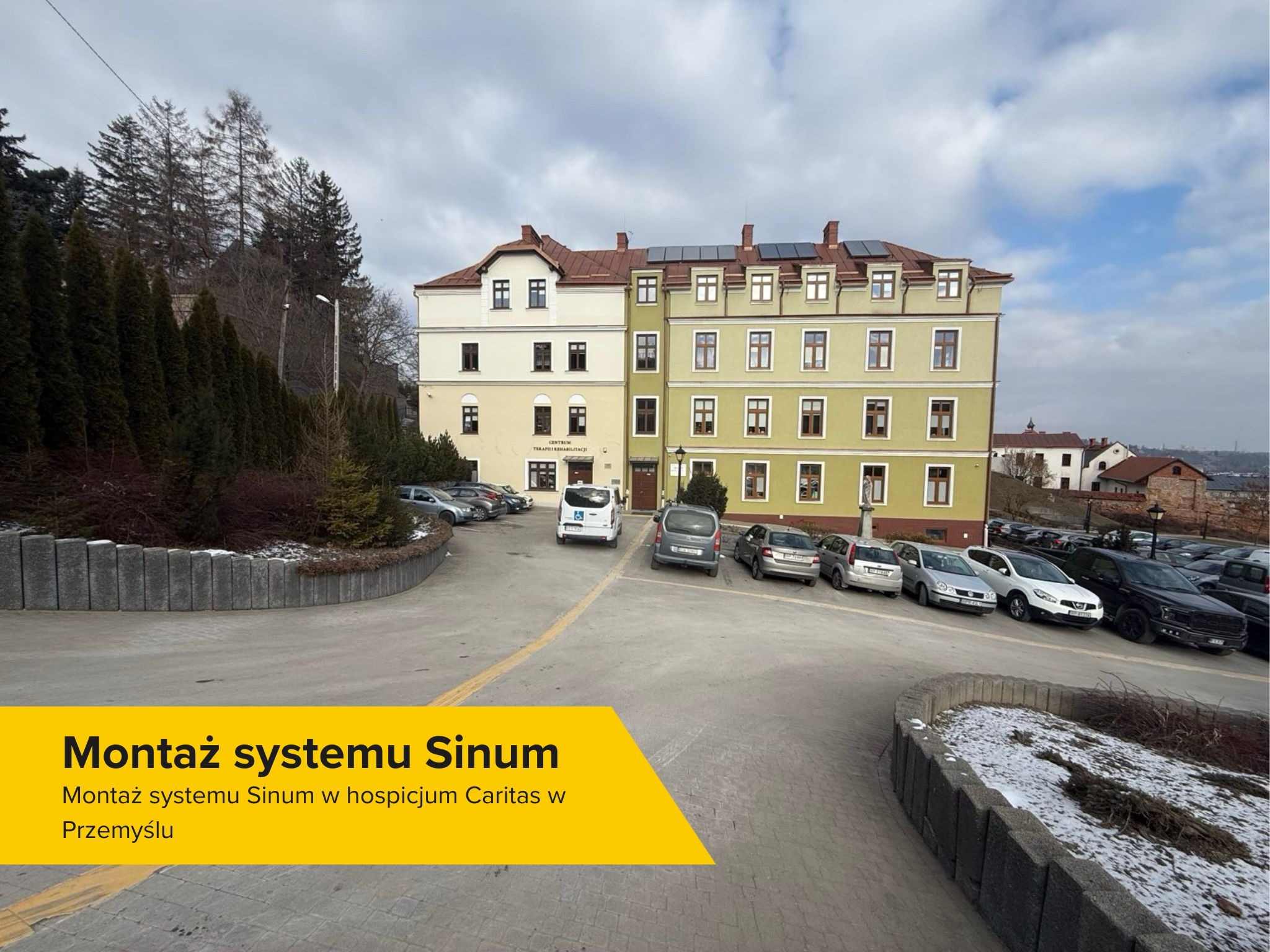 Budynek hospicjum Caritas w Przemyślu z panelami słonecznymi na dachu, widok z parkingu.
