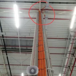 Wysoka kolumna z pomarańczowymi kablami prowadzonymi wzdłuż betonu, widoczne głośniki tubowe, instalacja w hali przemysłowej w Kielcach.