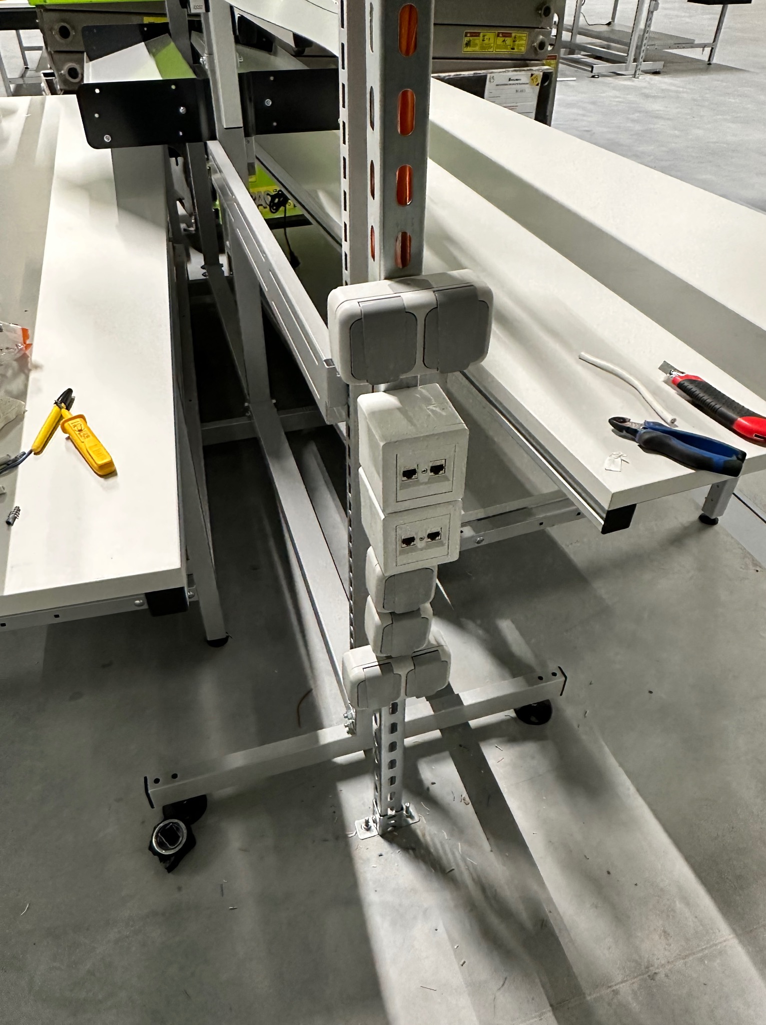 Montaż gniazd sieciowych w blacie roboczym, widoczne narzędzia: obcinak do kabli, nóż tapicerski, zaciskarka do wtyków RJ45.