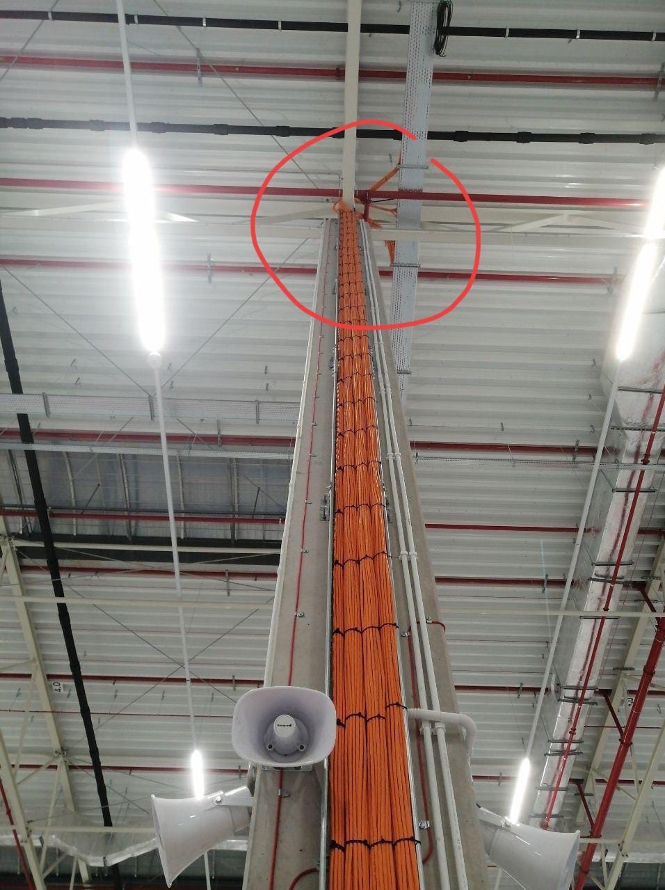 Wysoka kolumna z pomarańczowymi kablami prowadzonymi wzdłuż betonu, widoczne głośniki tubowe, instalacja w hali przemysłowej w Kielcach.
