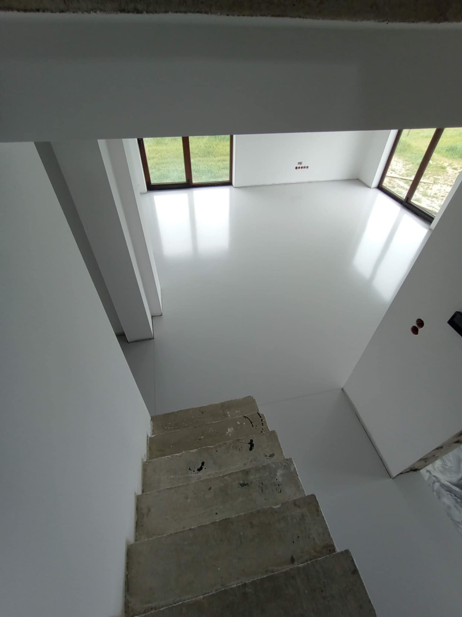 Jasne, lśniące wykończenie podłogi w nowym domu, widok z góry schodów, duże okna z widokiem na zieleń.