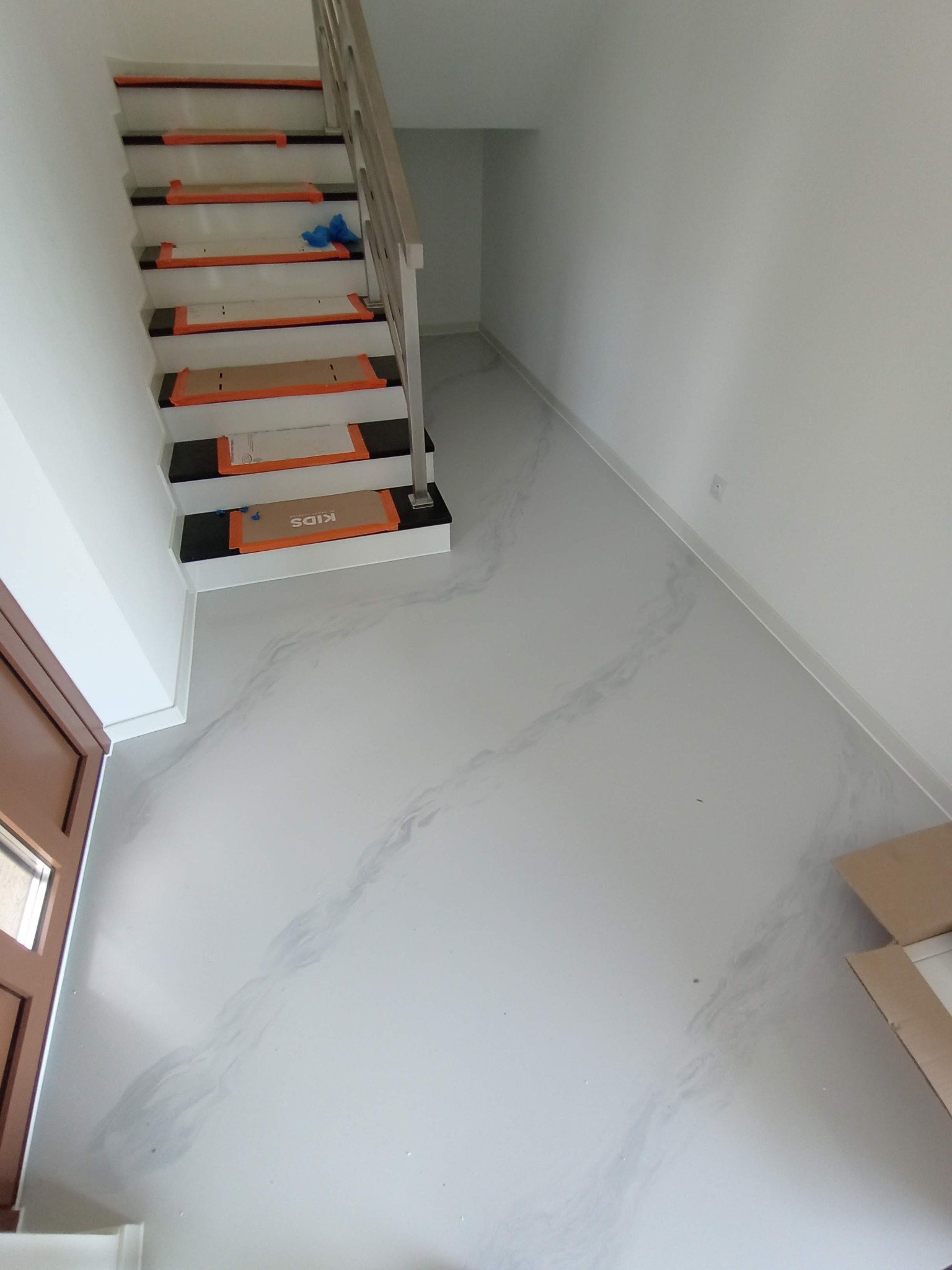 Biała posadzka z żywicy epoksydowej imitująca marmur, schody zabezpieczone kartonem i taśmą malarską, widok z góry.