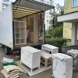 ANATOLII KUCHEREVSKYI - Załadunek mebli, zapakowanych w folię ochronną, do samochodu dostawczego w Bielsku-Białej. Widoczne komoda, regał, stolik i pralka, zabezpieczone koce i folia.