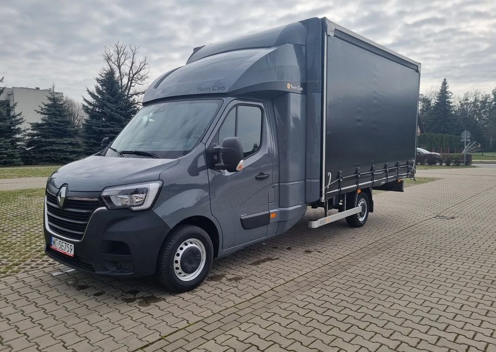 Szary samochód dostawczy Renault Master Twin Cab z plandeką, zaparkowany na kostce brukowej w pochmurny dzień.