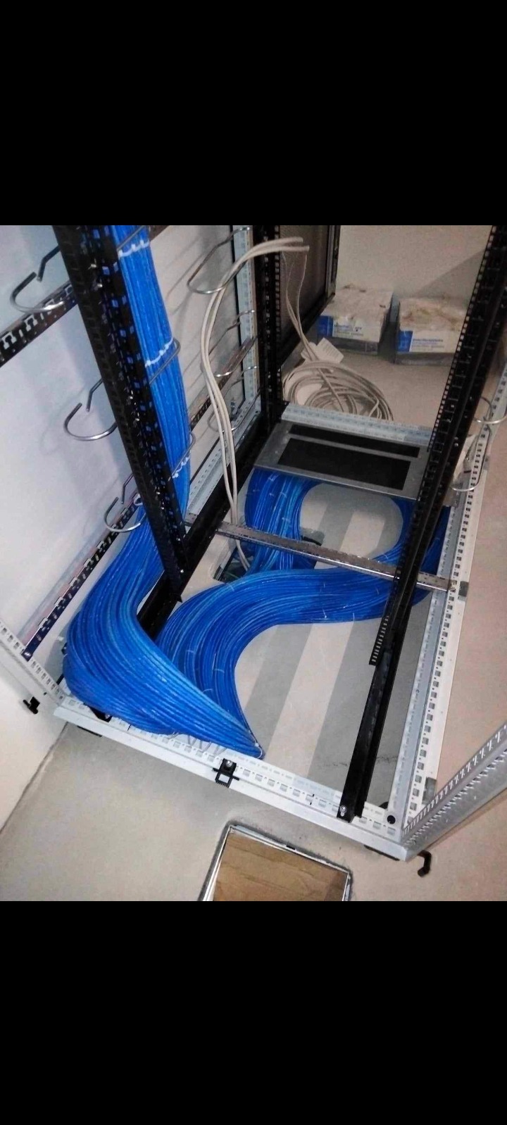 Szafa serwerowa z uporządkowanymi niebieskimi kablami sieciowymi, widoczne metalowe uchwyty i koryto kablowe, w tle fragment ściany i podłogi.