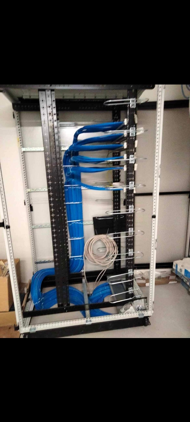 Szafa rack z uporządkowanymi niebieskimi kablami światłowodowymi i spiralą kabla koncentrycznego, widoczne elementy mocujące i konstrukcja szafy.
