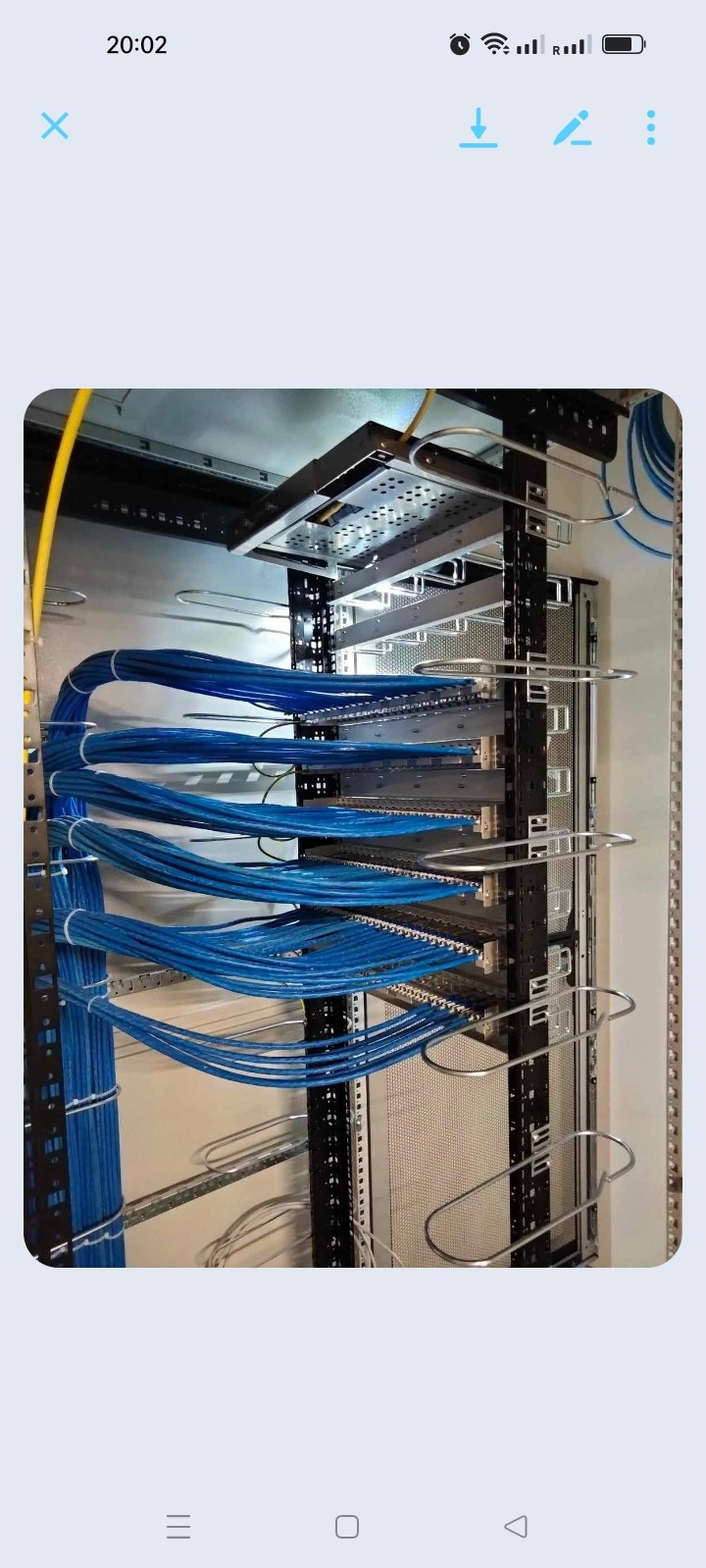 Rząd starannie ułożonych niebieskich kabli sieciowych w szafie rack, zabezpieczonych metalowymi uchwytami, z widocznymi panelami krosowniczymi i elementami montażowymi.