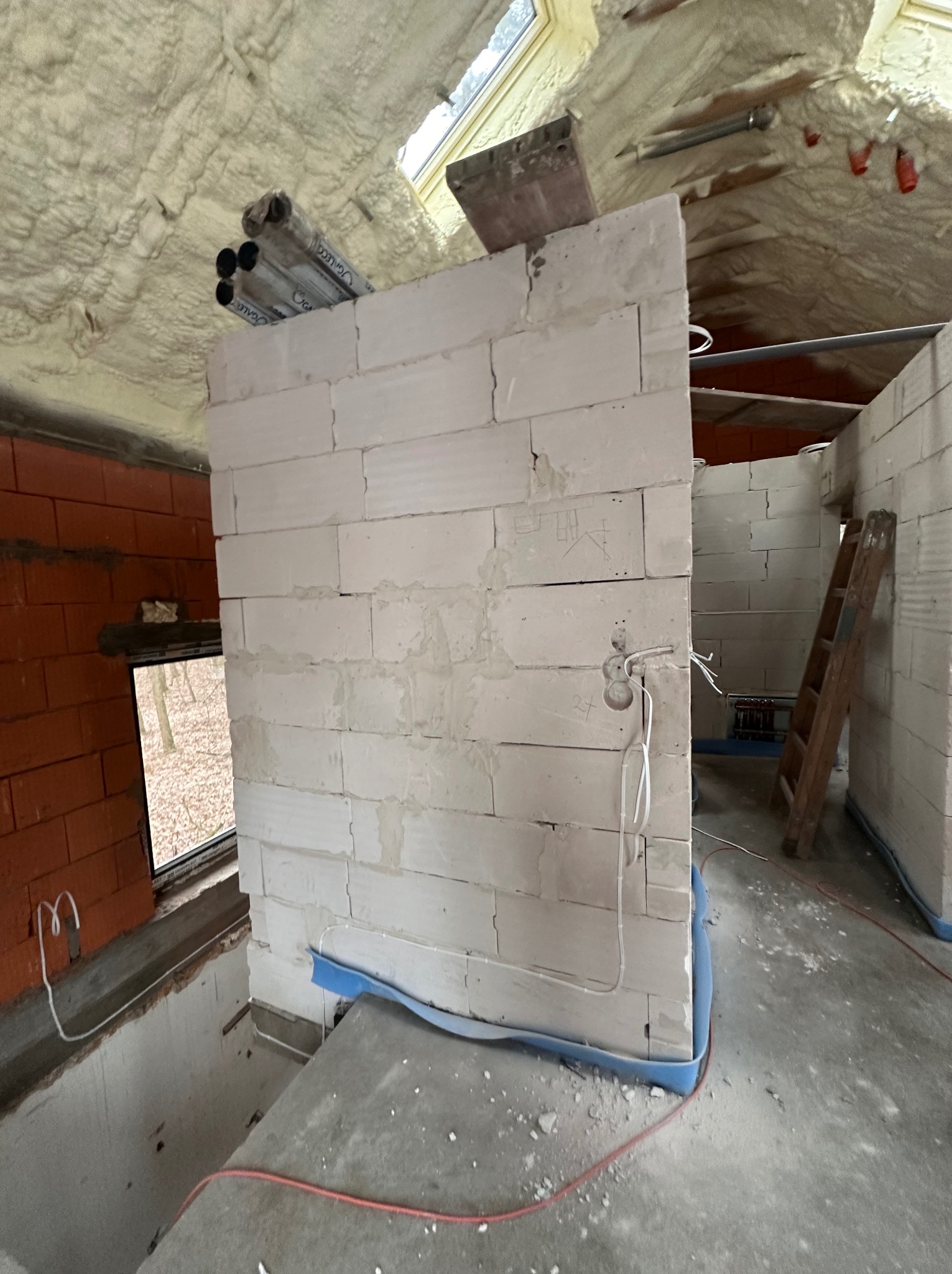 Wnętrze w trakcie budowy w Pomiechówku, widoczne ściany z białego bloczka, ocieplony pianą sufit z rurami instalacyjnymi oraz wystające przewody elektryczne ze ściany.