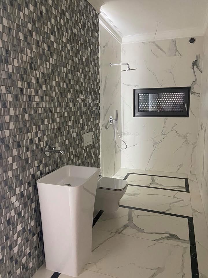 Nowoczesna łazienka w Wieluniu z białą umywalką na postumencie, mozaikową ścianą i marmurowym wykończeniem podłogi z czarnymi akcentami.