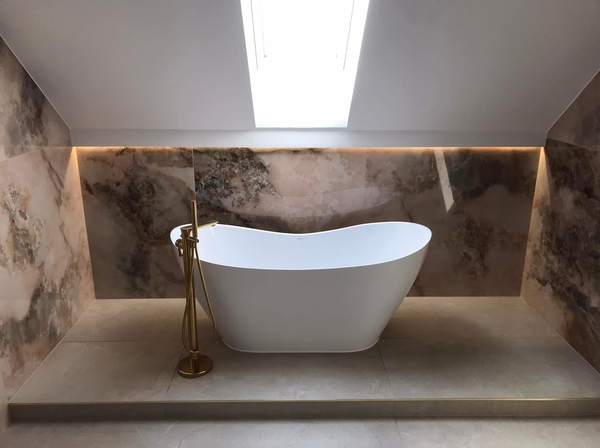 Nowoczesna, wolnostojąca wanna w łazience na poddaszu z oknem dachowym, wykończonej płytkami imitującymi marmur i podświetleniem LED.