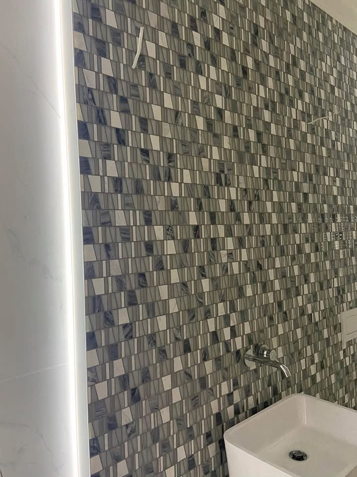 Ściana w łazience wyłożona mozaiką w odcieniach szarości i bieli, z nowoczesną umywalką i minimalistyczną baterią, oświetlona pionowym pasem ledowym.