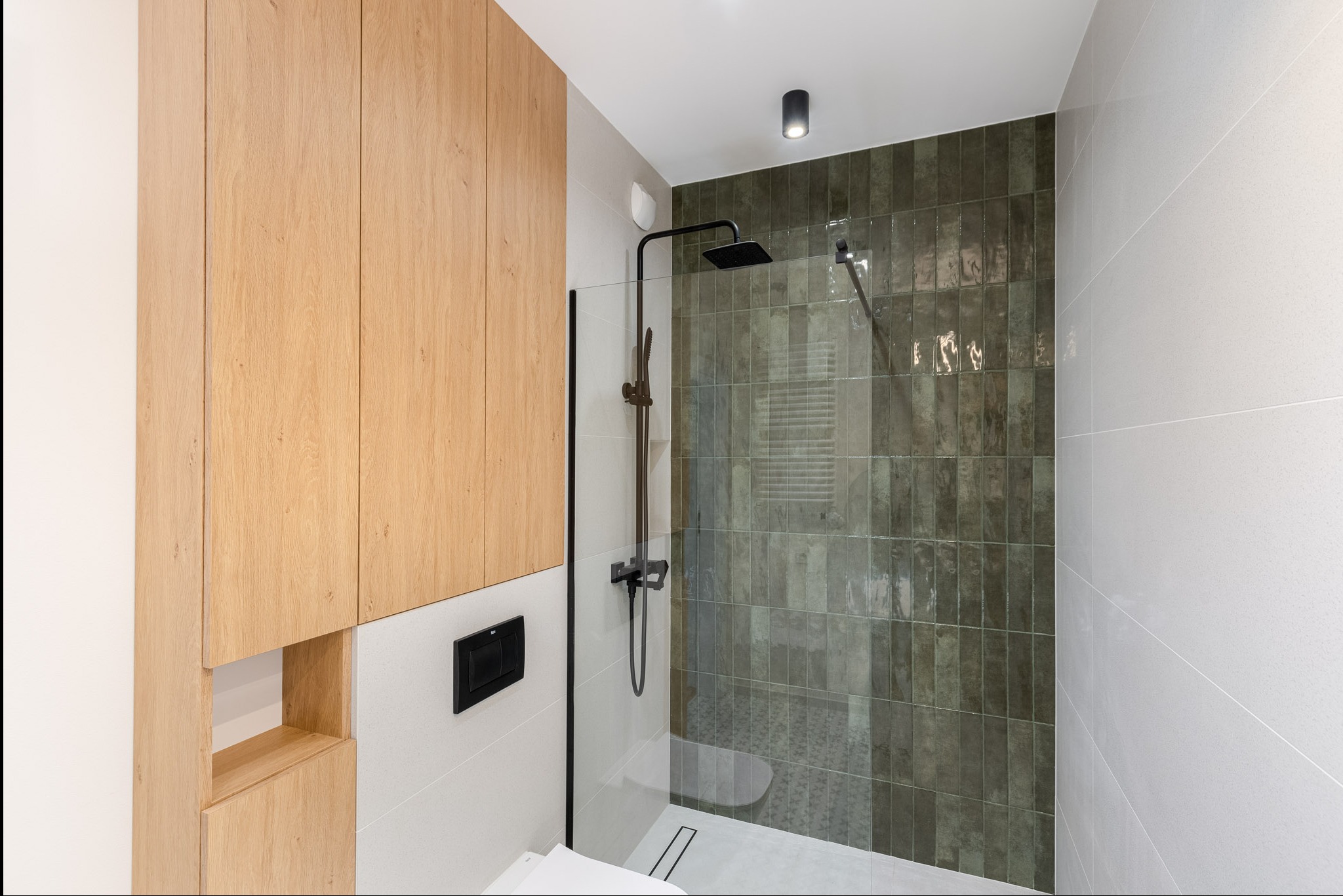 Nowoczesna łazienka z kabiną prysznicową typu walk-in, wykończona płytkami w odcieniach zieleni i drewna, czarna armatura, minimalistyczny design.