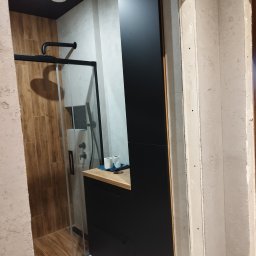 Vibe Wood - Nowoczesna łazienka z kabiną prysznicową typu walk-in, czarną szafką z drewnianym blatem, wykończona w drewnie i szarości, widok z surowego otworu drzwiowego.