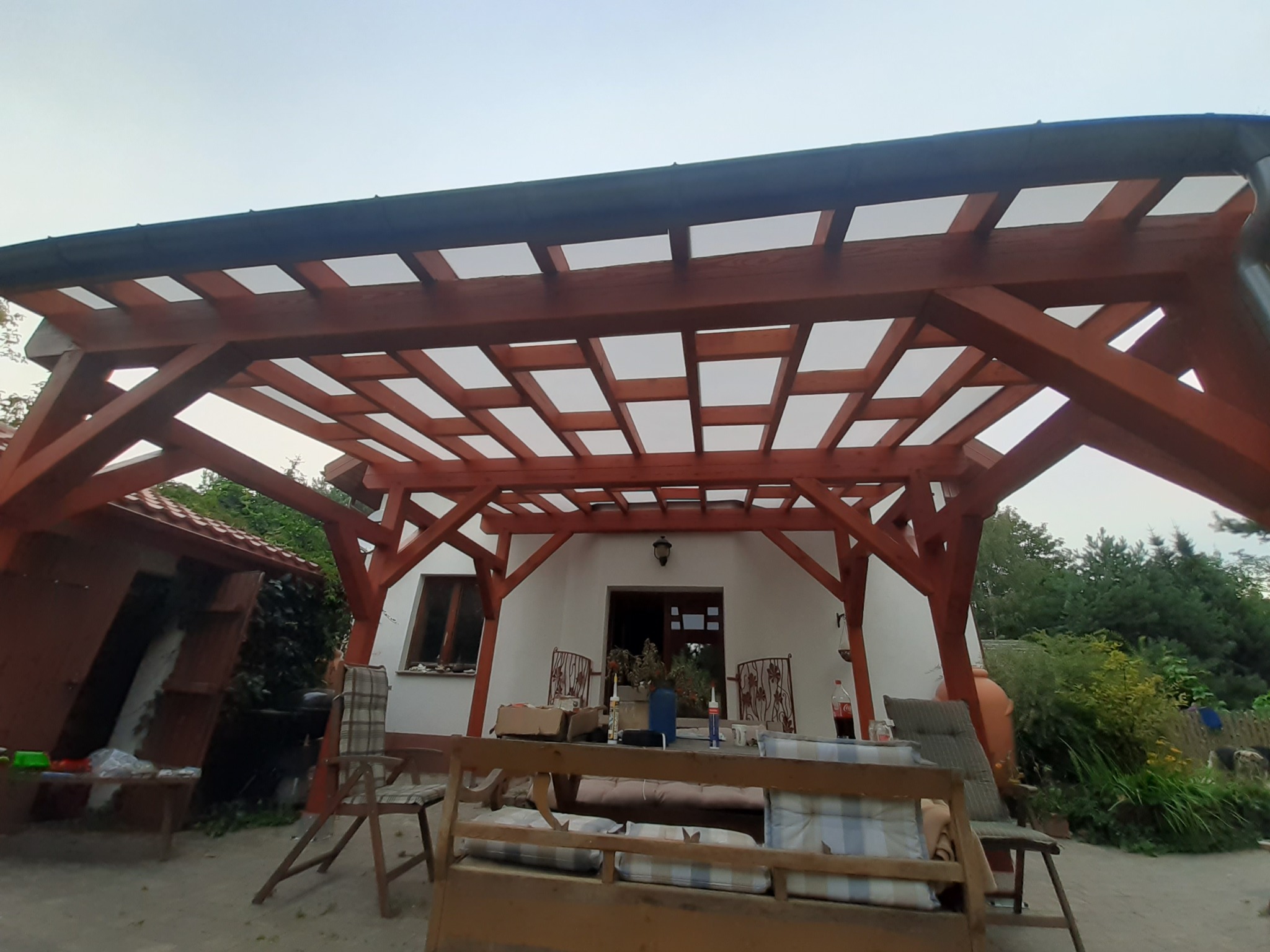 Drewniana konstrukcja z przezroczystym zadaszeniem, prawdopodobnie w trakcie budowy, z widocznymi elementami wyposażenia i narzędziami na stole w tle.