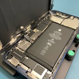 iBroken - Serwis Apple Kraków - Otwarty iPhone na uchwycie serwisowym, widoczna bateria, płyta główna i inne komponenty wewnętrzne podczas naprawy.