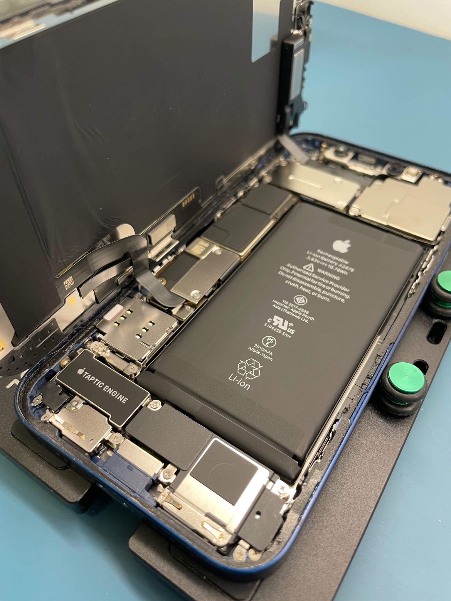 Otwarty iPhone na uchwycie serwisowym, widoczna bateria, płyta główna i inne komponenty wewnętrzne podczas naprawy.