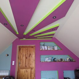 PPUH Pierlak szymon - Poddasze po remoncie z fioletowymi ścianami, drewnianymi półkami i drzwiami oraz oryginalnym sufitem w pasy fioletu, bieli i zieleni z wbudowanym oświetleniem.