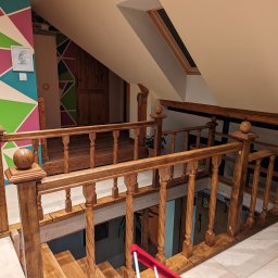 PPUH Pierlak szymon - Drewniane schody i balustrada z toczonymi elementami w jasnym wnętrzu poddasza, widoczne okno dachowe i dekoracyjna ściana z geometrycznym wzorem w tle.