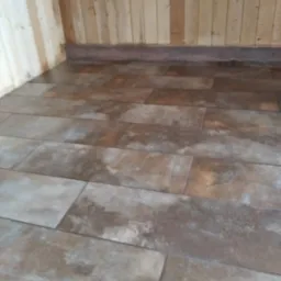 Wykończone wnętrze z drewnianą boazerią i podłogą wyłożoną brązowymi płytkami imitującymi drewno.