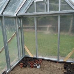 PPUH Pierlak szymon - Wnętrze szklarni z metalową konstrukcją i przezroczystym pokryciem, z widocznymi doniczkami z ziemią przygotowanymi do sadzenia roślin.