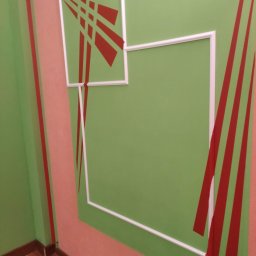 PPUH Pierlak szymon - Wykończone wnętrze: zielone ściany z dekoracyjnymi, czerwonymi pasami i białymi ramkami w narożniku pokoju, drewniana podłoga.