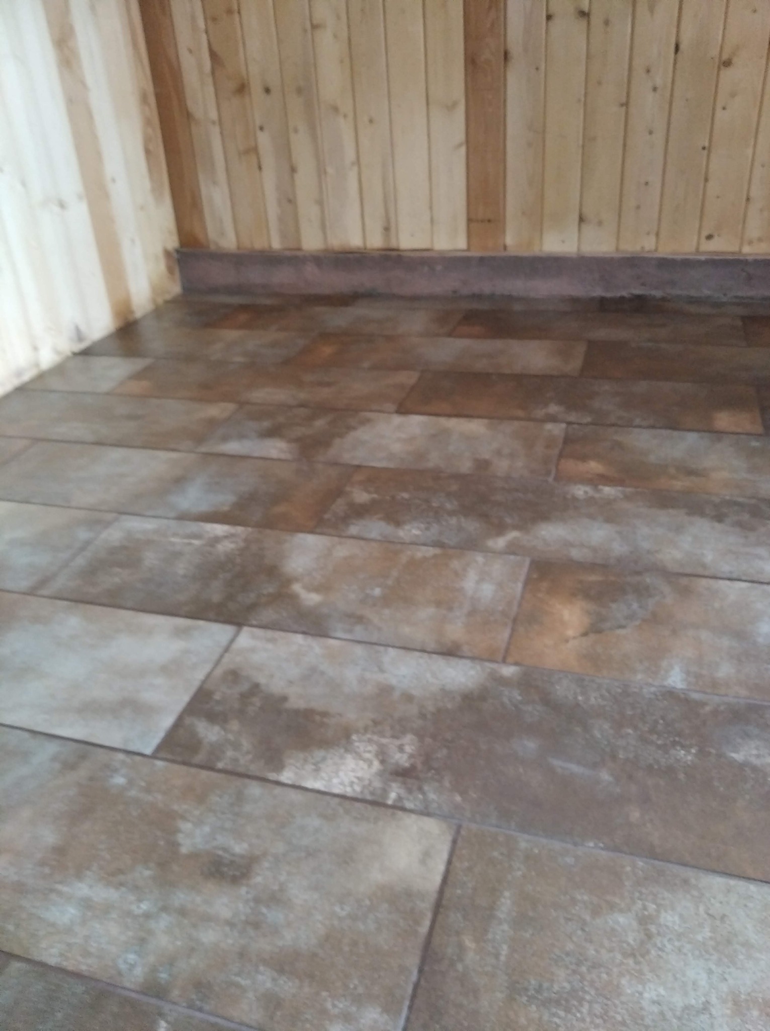 Wykończone wnętrze z drewnianą boazerią i podłogą wyłożoną brązowymi płytkami imitującymi drewno.