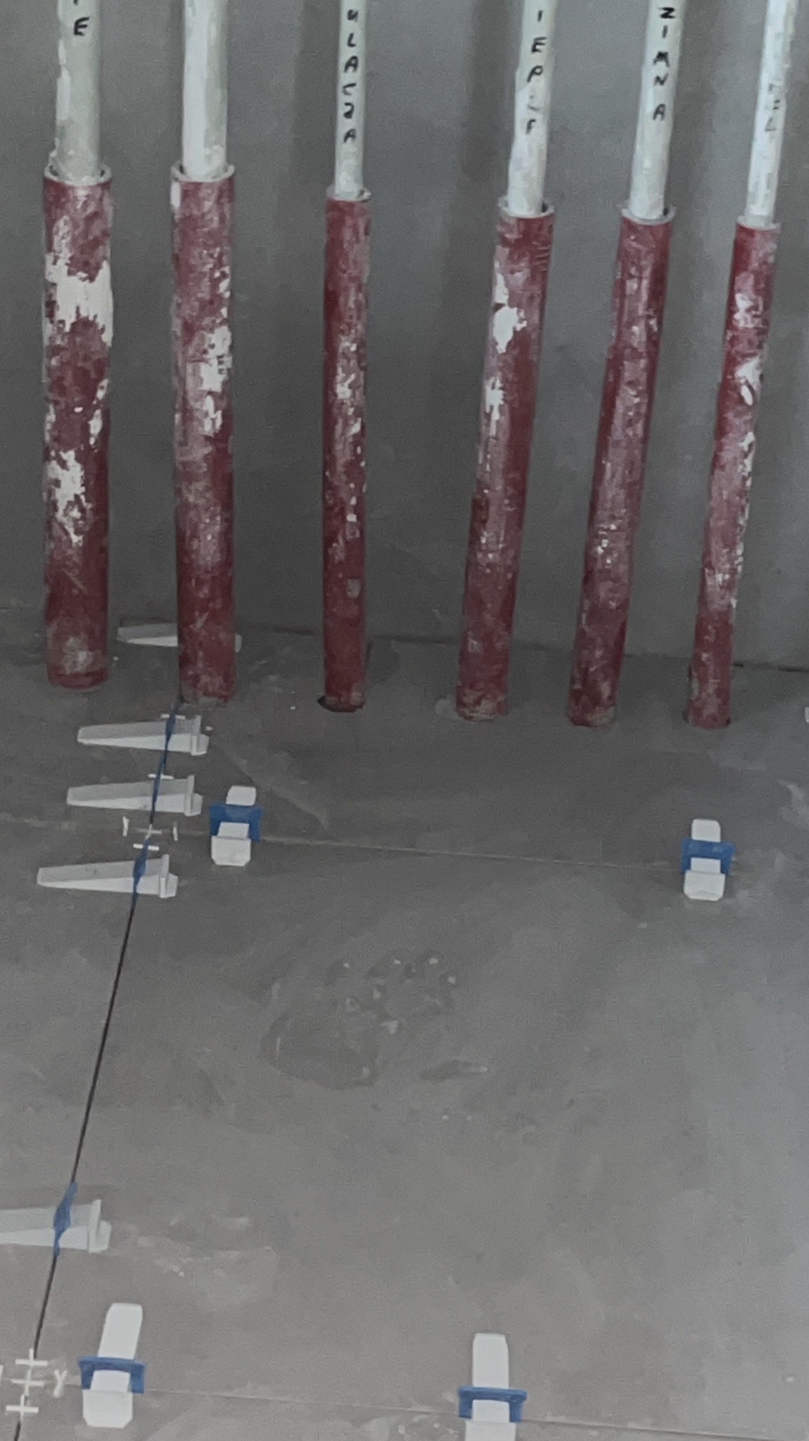 Przygotowanie podłoża pod płytki w łazience: rury z instalacją wystające ze ściany, poziomowanie podłoża za pomocą sznurka i plastikowych krzyżyków dystansowych.