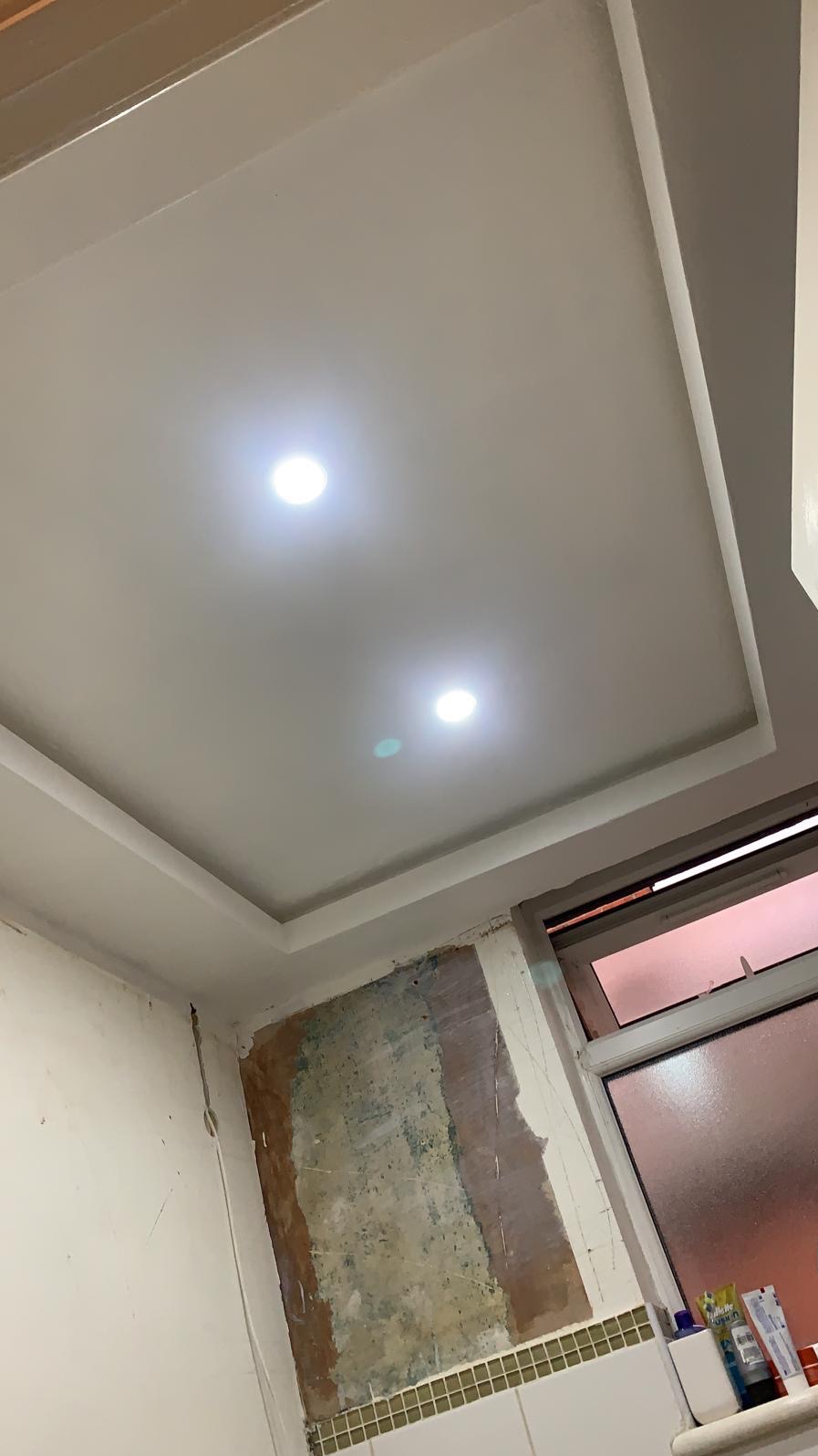 Przygotowana do malowania sufit i ściany łazienki z widocznymi śladami po wcześniejszych pracach, dwa wbudowane punkty świetlne, okno z widocznymi kosmetykami na parapecie.