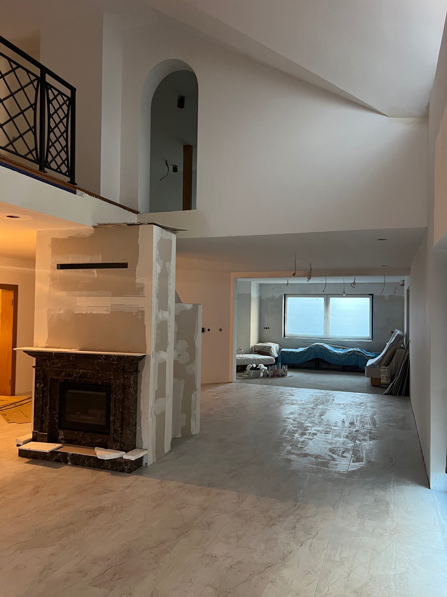 Wnętrze w trakcie remontu: widoczny kominek z ciemnego marmuru, świeżo położona, błyszcząca podłoga z płytek imitujących marmur, ściany przygotowane do malowania, widoczne płyty gipsowo-kartonowe...