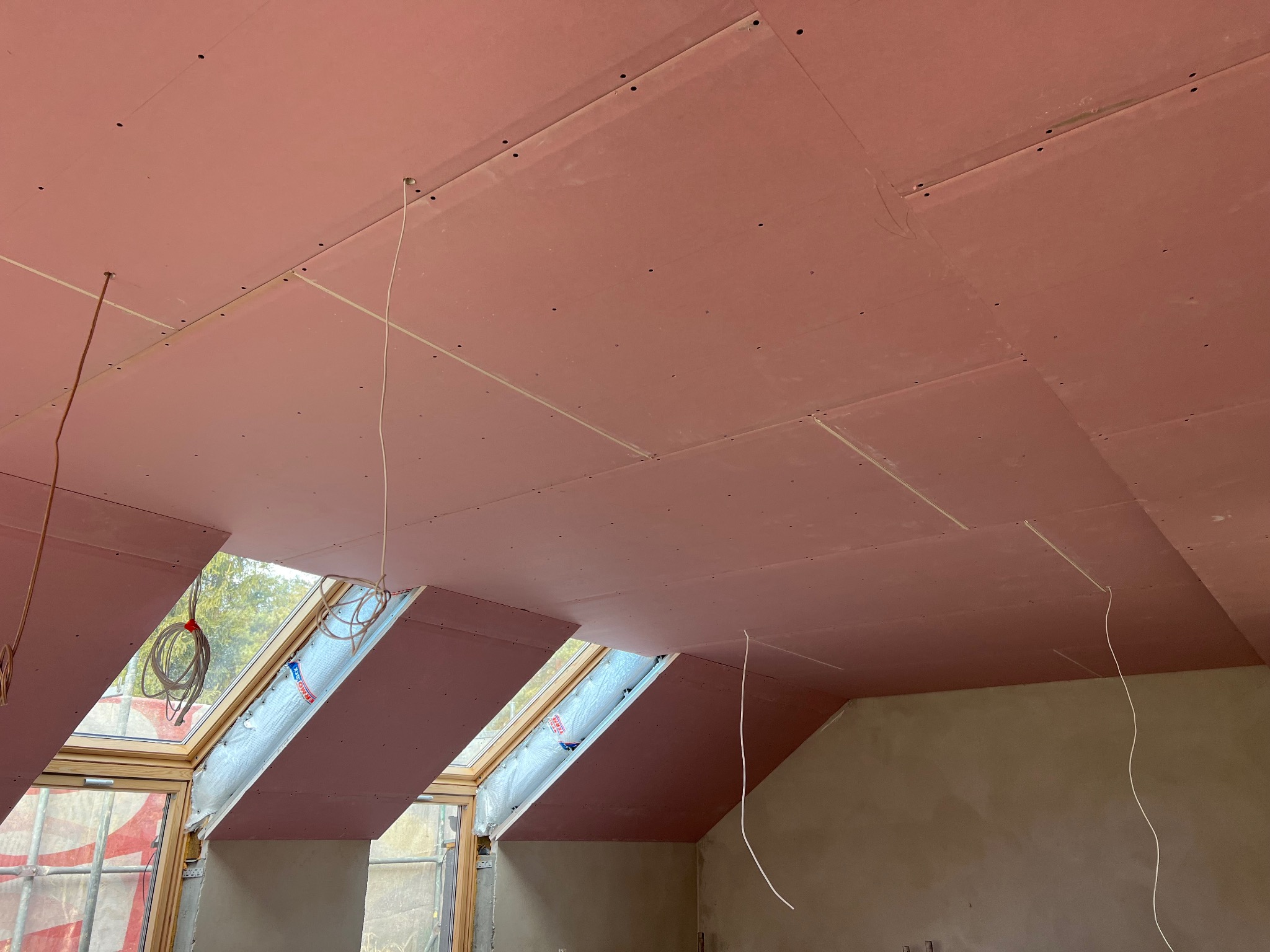 Montaż płyt gipsowo-kartonowych na poddaszu w Bochni, widoczne okna dachowe z folią ochronną i wystające przewody elektryczne.