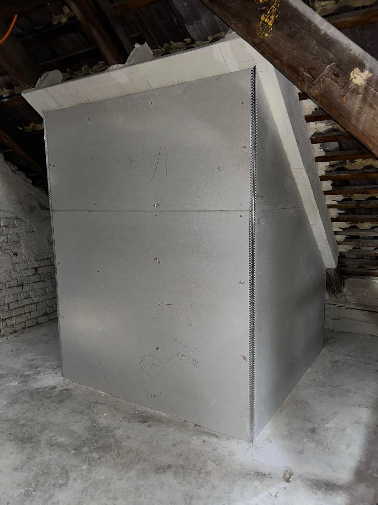 Konstrukcja z płyt kartonowo-gipsowych w trakcie montażu na poddaszu, widoczne profile narożnikowe, surowy stan, ślady ołówka na powierzchni.