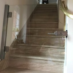 Alhen Artszkło Sp. z o.o. - Szklana barierka zabezpieczająca schody z marmurowymi stopniami, zamontowana na zawiasach z metalowymi okuciami, z widoczną klamką i zamkiem na górze.