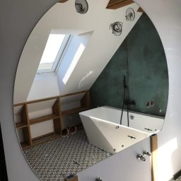 Alhen Artszkło Sp. z o.o. - Owalne lustro odbijające wnętrze łazienki na poddaszu z wanną, półkami i wzorzystą podłogą, widok z perspektywy montażu armatury.