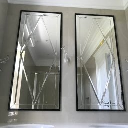 Alhen Artszkło Sp. z o.o. - Dwa prostokątne lustra z geometrycznym wzorem w czarnych ramach, zamontowane nad białą umywalką w łazience z jasnymi płytkami.