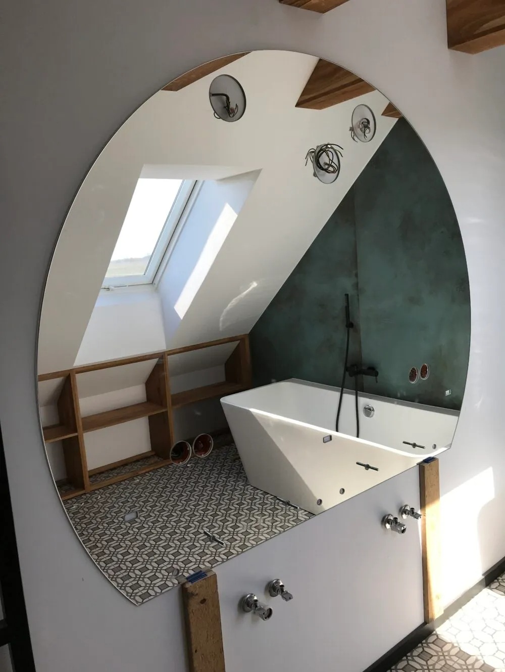Owalne lustro odbijające wnętrze łazienki na poddaszu z wanną, półkami i wzorzystą podłogą, widok z perspektywy montażu armatury.